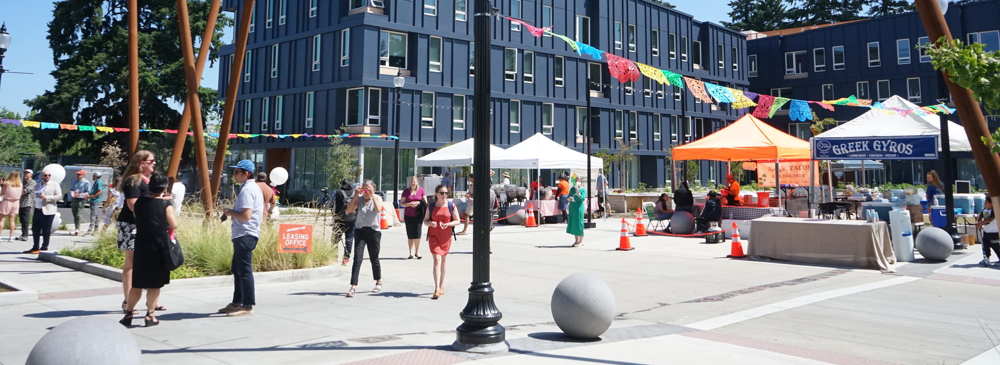 A crowd of people gather and enjoy a variety of food cards and info booths in the courtyard of the affordable housing project Rockwood Village in Gresham on a sunny day.