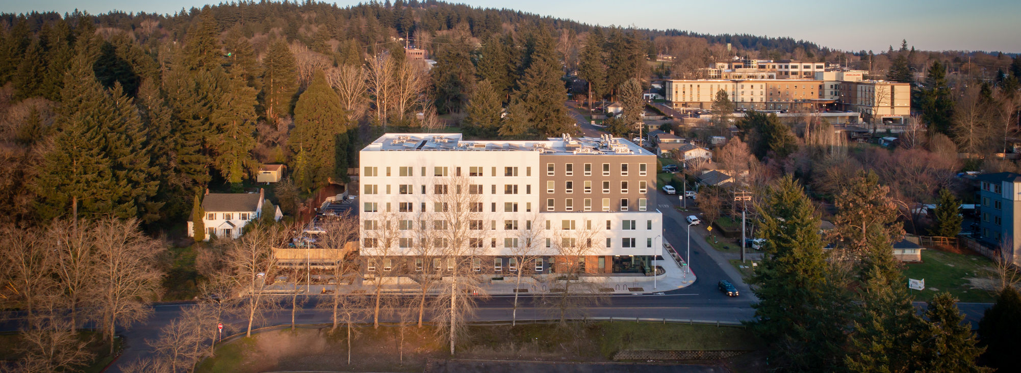 Aerial view of affordable housing project Viewfinder apartments in Tigard, with the setting sun illuminating the 6-story gray and white building.