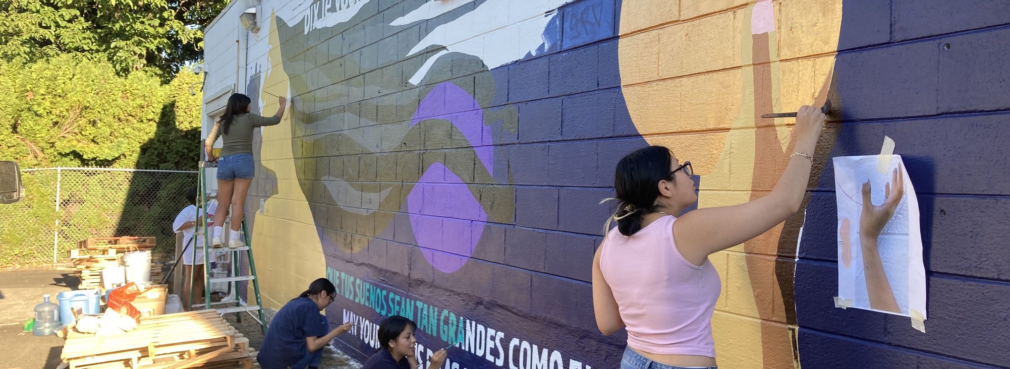 Youth painting a mural on the side of a building for the Mayan Culture and Tradition Fest