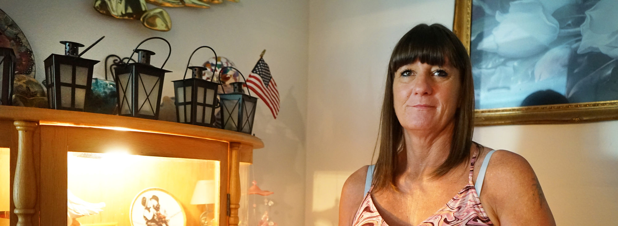 Woman in pink blouse standing by cabinet with small decorative objects