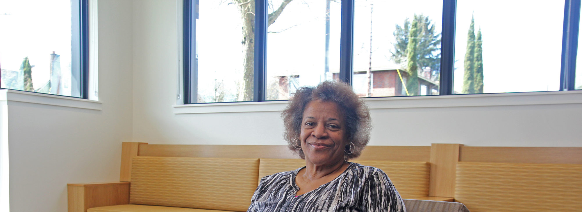 Portrait of an elder woman with short hair and a striped blouse smiling, sitting in a lounge area
