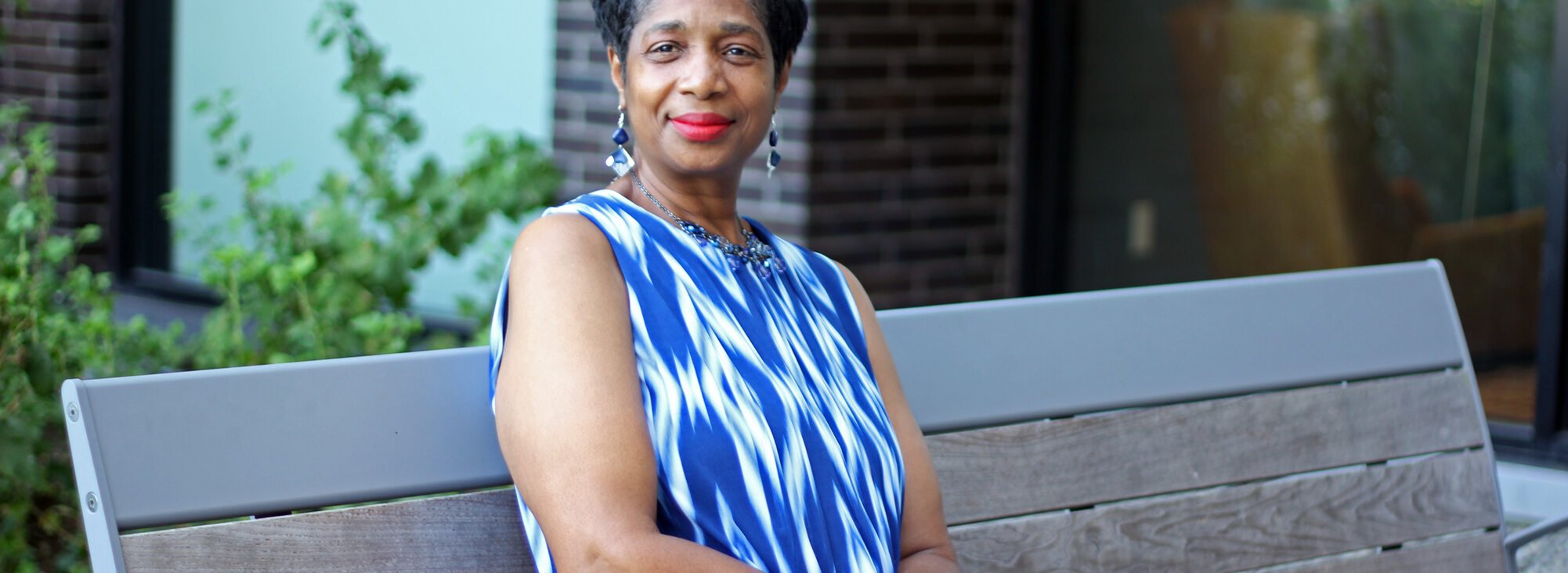 Woman with short dark hair and a blue print dress sitting on a bench