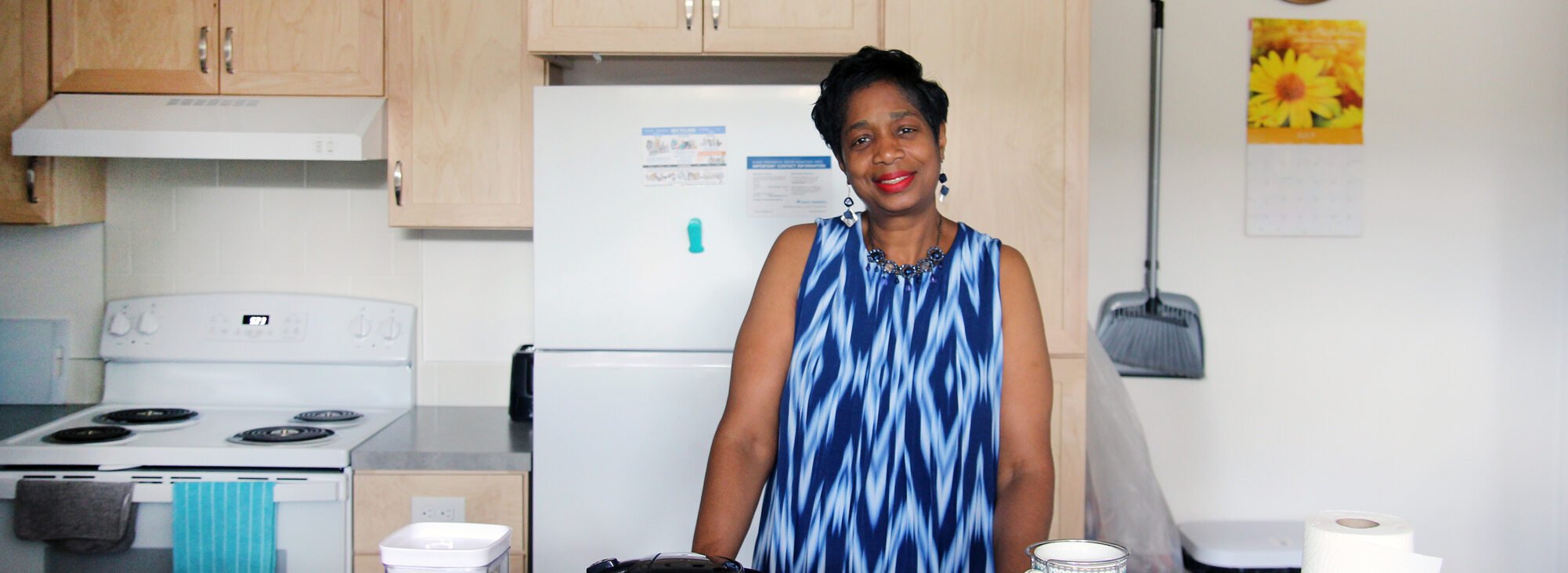 Woman with short dark hair and a blue print dress standing in her kitchen