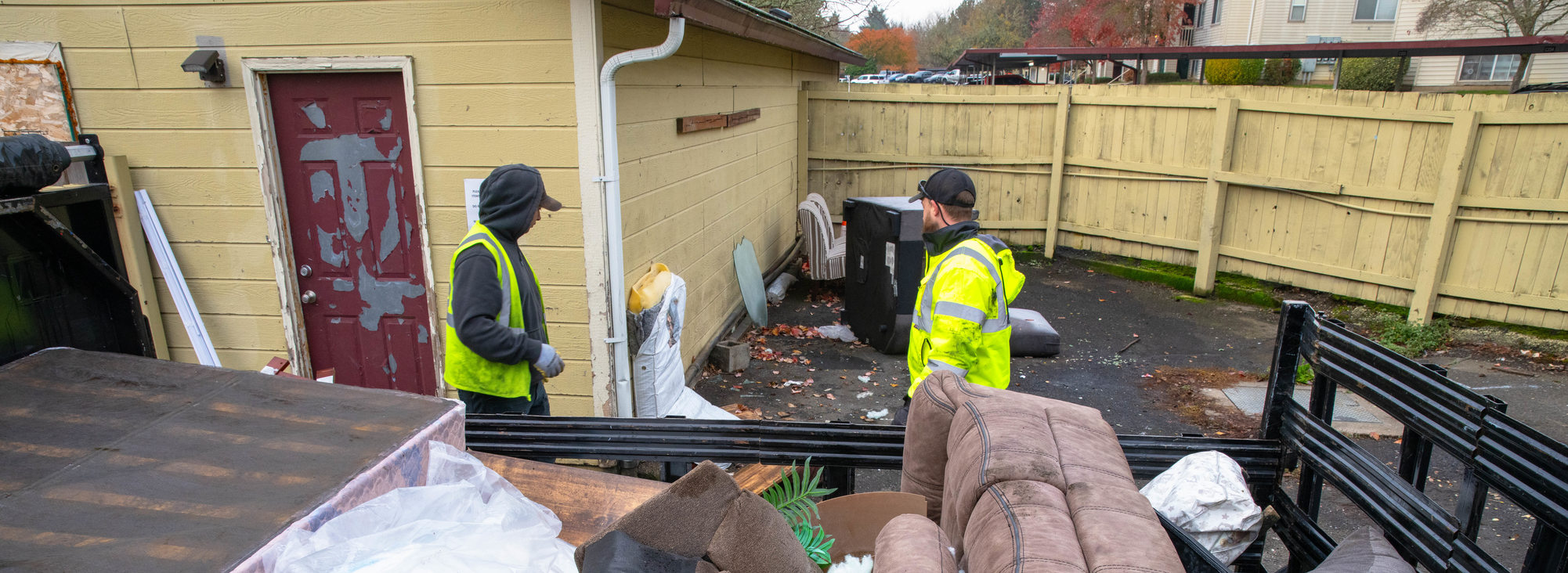 Overhead view of full trailer hall with couches and other furniture while waste management haulers collect more discarded items in an apartment complex.