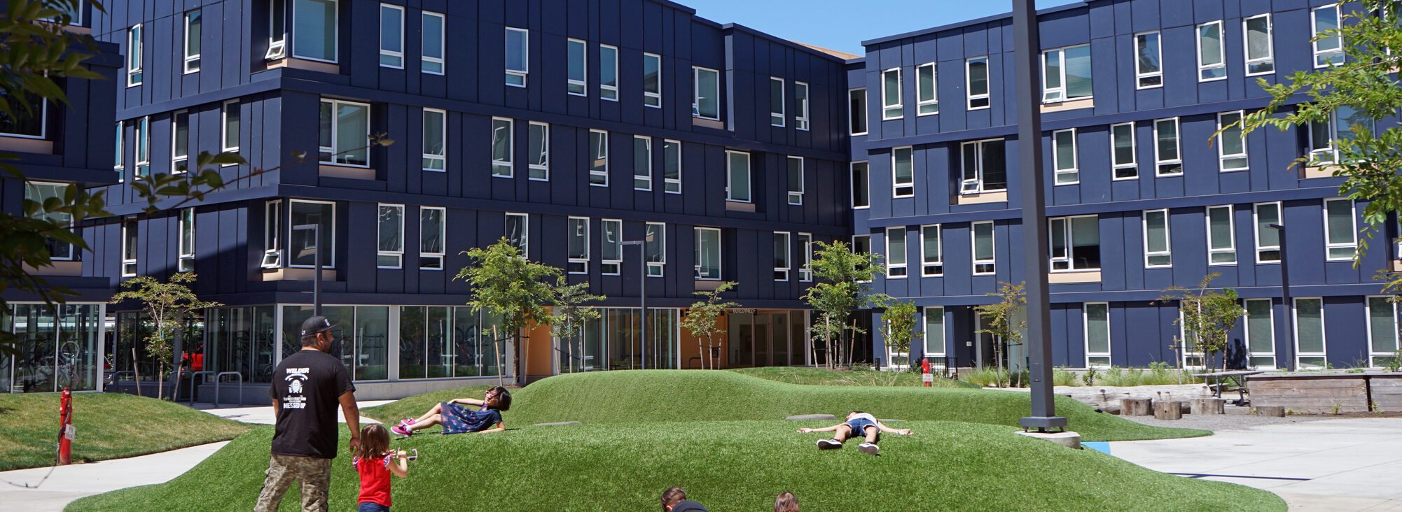 Children play on a sloping green lawn feature in front of the Rockwood Village housing complex. 