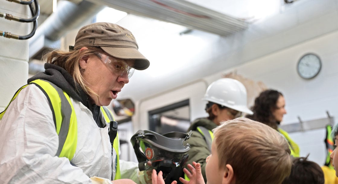 a woman in protective gear hands out gas masks to a group of kids