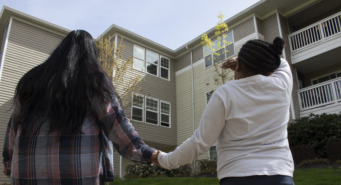 woman and daughter holding hands and looking at an apartment building