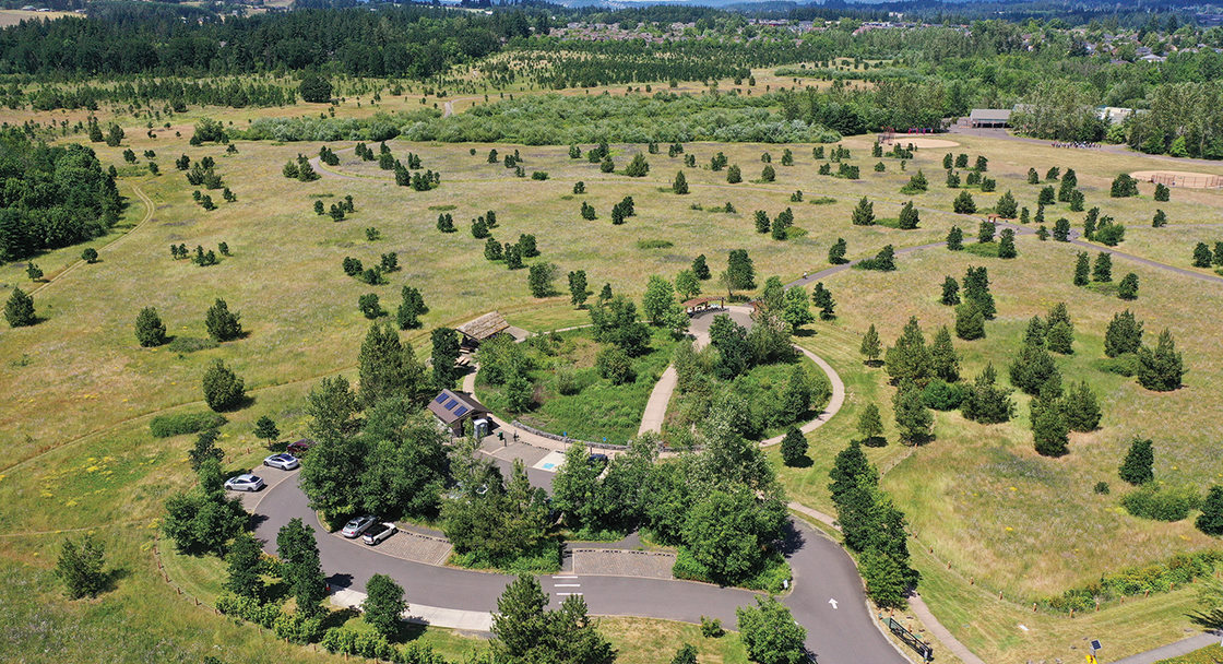 From an aerial view, a park with a large prairie and few trees stretches towards more forested areas.