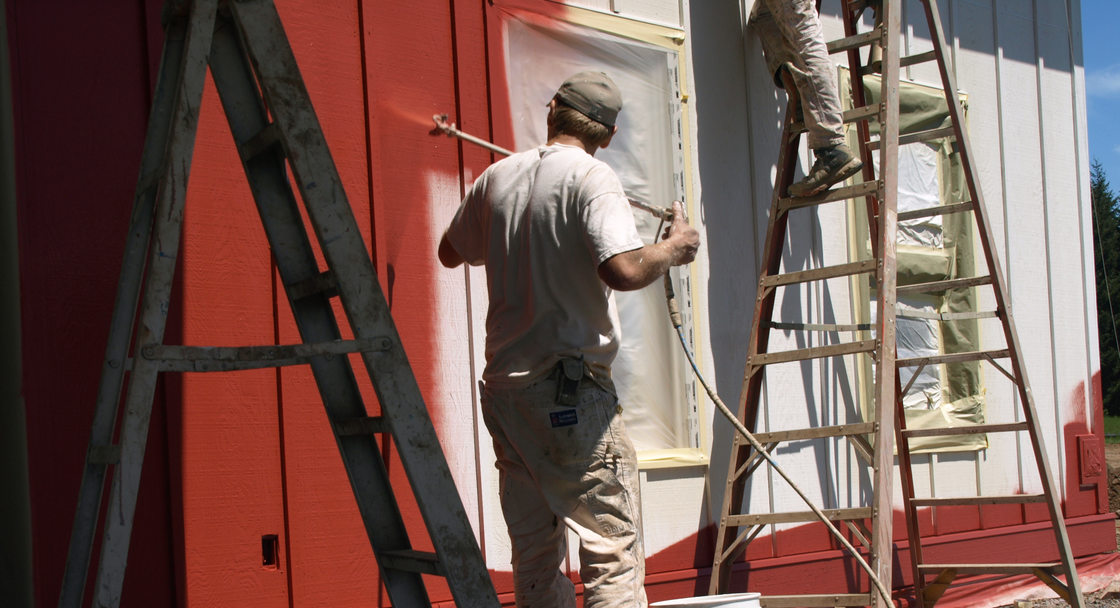 An image of two people painting a house red