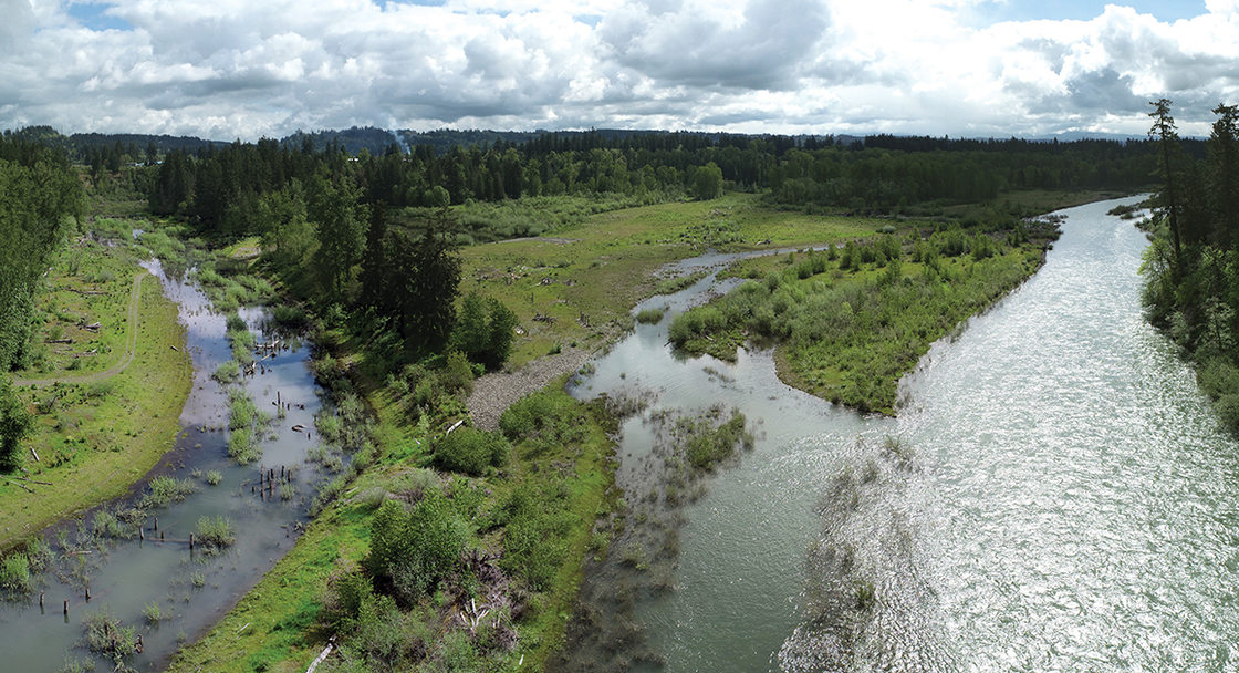 In a drone image, a large river meets a smaller one, with green, tree-filled fields between them.