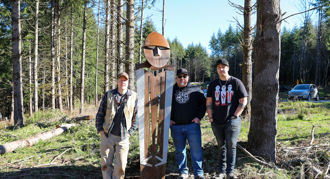 Three artists stand next to a statue at a park.