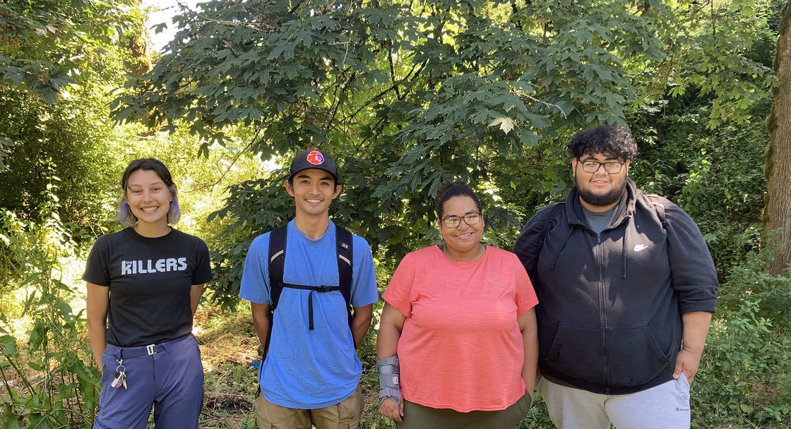 Four youth stand in front of a beautiful forest background