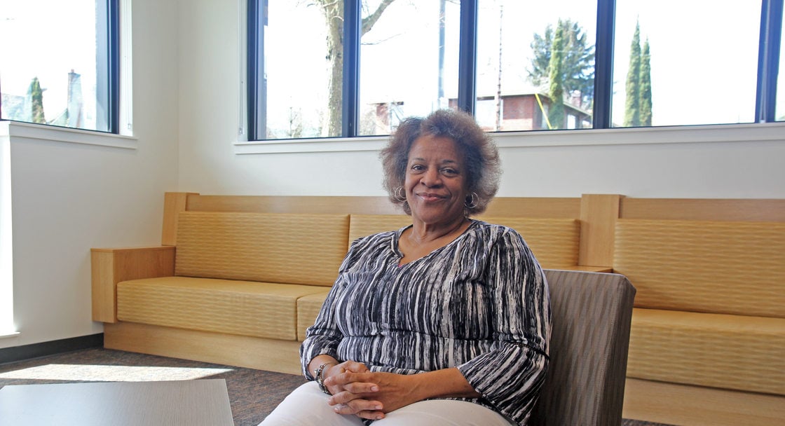 Portrait of an elder woman with short hair and a striped blouse smiling, sitting in a lounge area