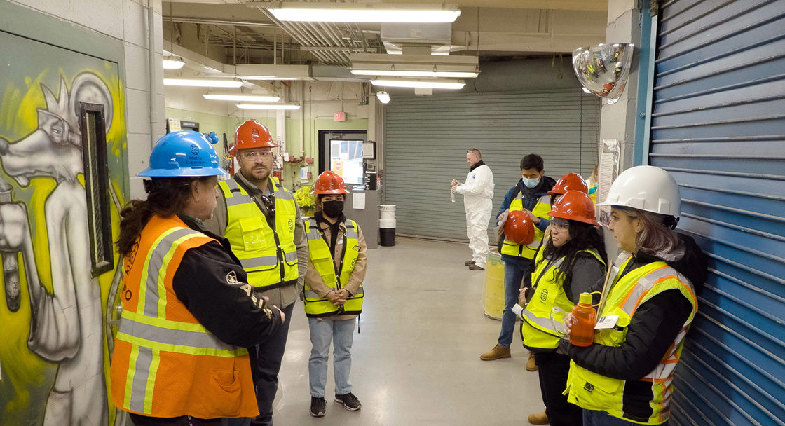 Group in safety vests and hardhats stand in a hallway of a hazardous waste disposal facility