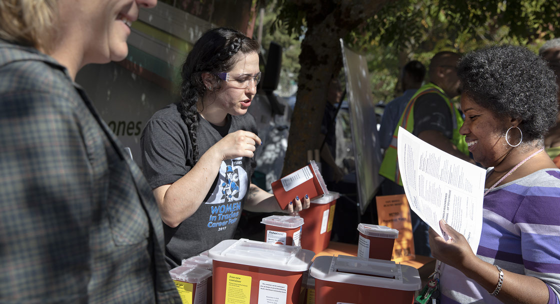 Three people gather around a table full of red medical sharps disposal boxes