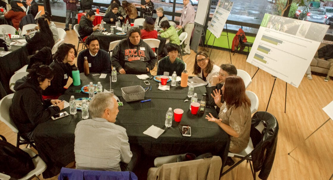 Members of Metro's Public Engagement Review Committee sit and talk around a round table in a conference room with visual props mounted on easels in the background.