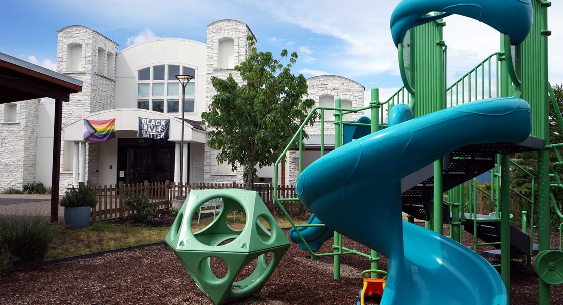 Blue and green playground in the foreground, with white multi-story building in the background. 