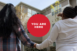 A woman and her daughter hold hands in front of an apartment building
