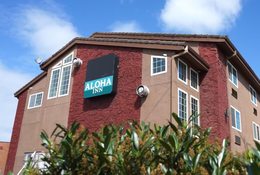 Aloha Inn affordable housing project in Washington County, showing the 3-story building in shades of brown and beige with a teal-colored sign reading Aloha Inn on the side of the building