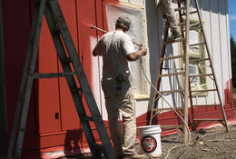 An image of two people painting a house red
