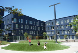 Children playing on a grass mound in front of dark blue multifamily housing