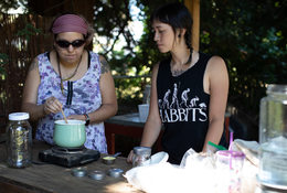 two people who are part of Atabey Medicine Council stand at a wooden table while one of them stirs the plant medicine from the ingredients they gathered earlier