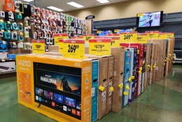 18 boxes of new televisions on a sales floor. Each TV has a bright yellow price tag with the sale price